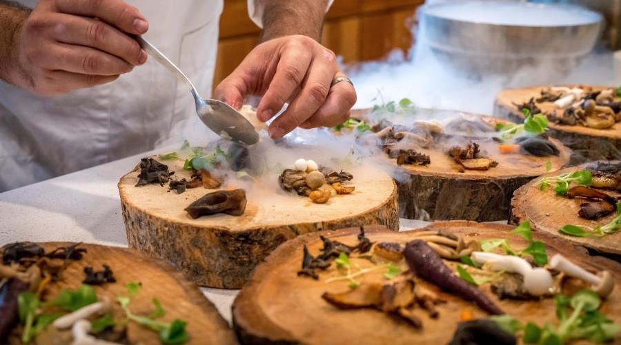 The chef at LucAle meticulously arranges various mushrooms on the wooden plate.